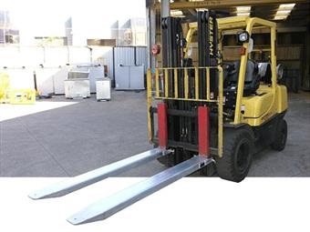 Yellow forklift fitted with a pair of forklift extension slippers.